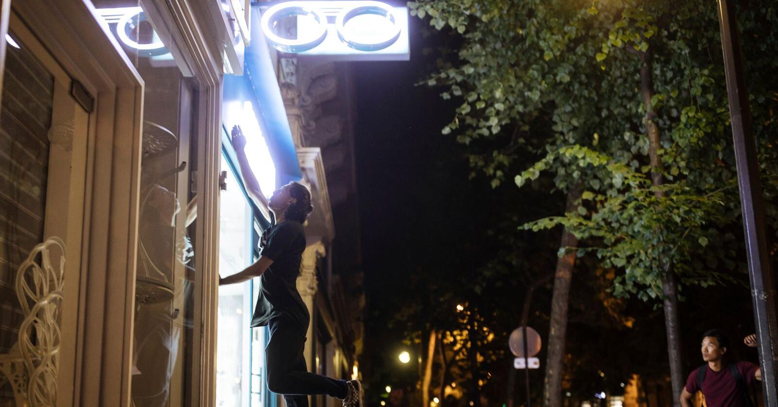 Hadj Benhalima fra kollektivet On the Spot hopper opp for å slå av lysene på en butikk under et nattlig tokt i Paris for å spare energi. Gruppen er urbane miljøvernere som har som mål å bekjempe energisløsing ved å slå av butikklys som står på om natta. Foto: Lewis Joly / AP / NTB