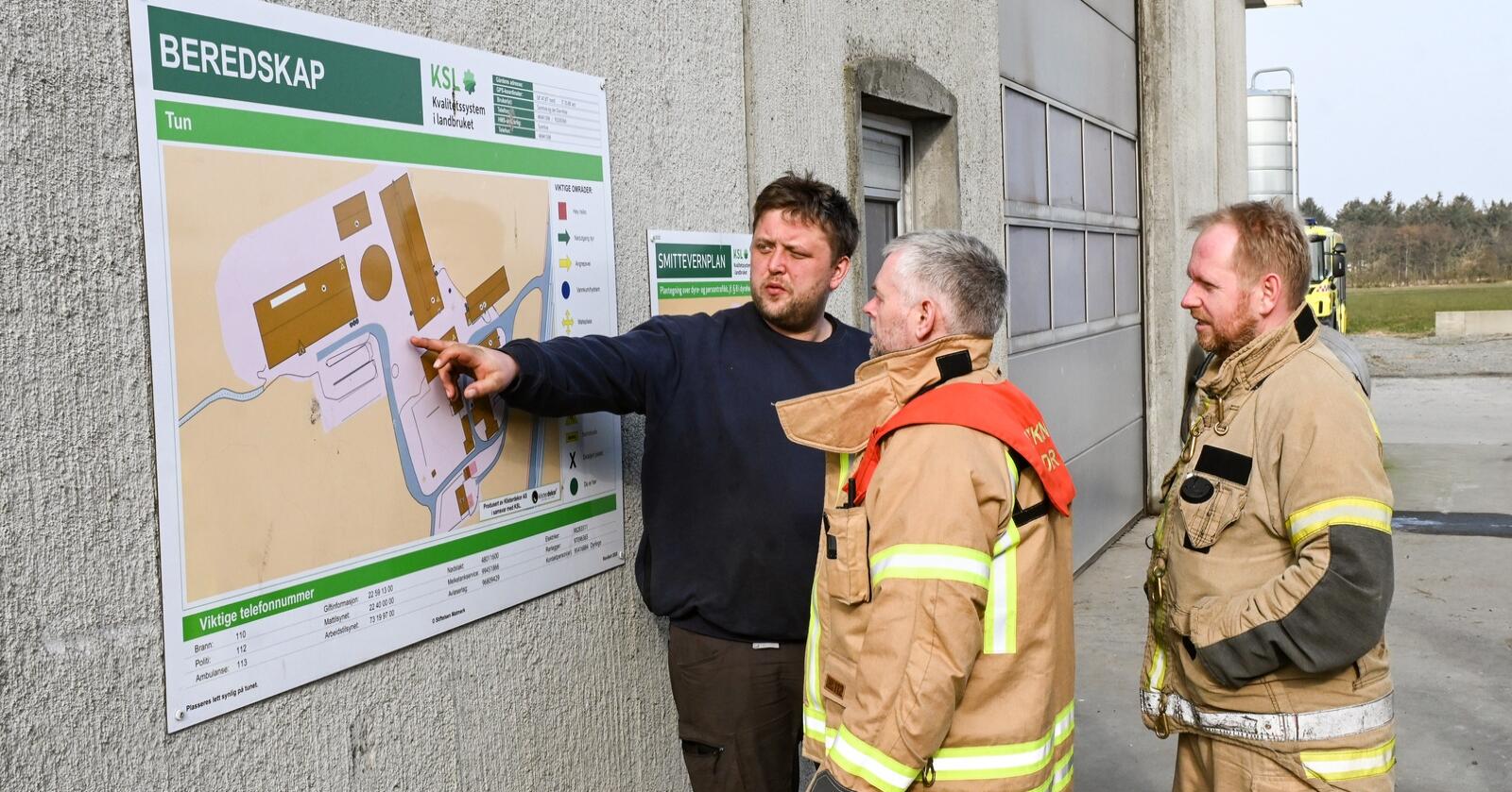 Jan Ove Hole viser frem plakatene for gårdens beredskap og smittevernplan til brannmester Rune Nedrebø og Stian Anda.