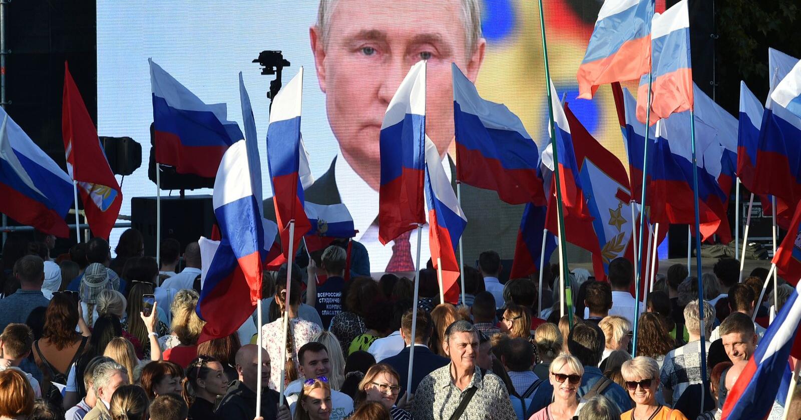Vladimir Putins bilde på en storskjerm bak russiske flagg under den storstilte feiringen av at Russland har annektert nye regioner fredag. Dagen etter gikk russerne på et nytt nederlag i Ukraina. Foto: AP / NTB